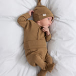 Baby iført brune ribstrikkede babybukser med nedbukket kant og futter, babybody og babyhue