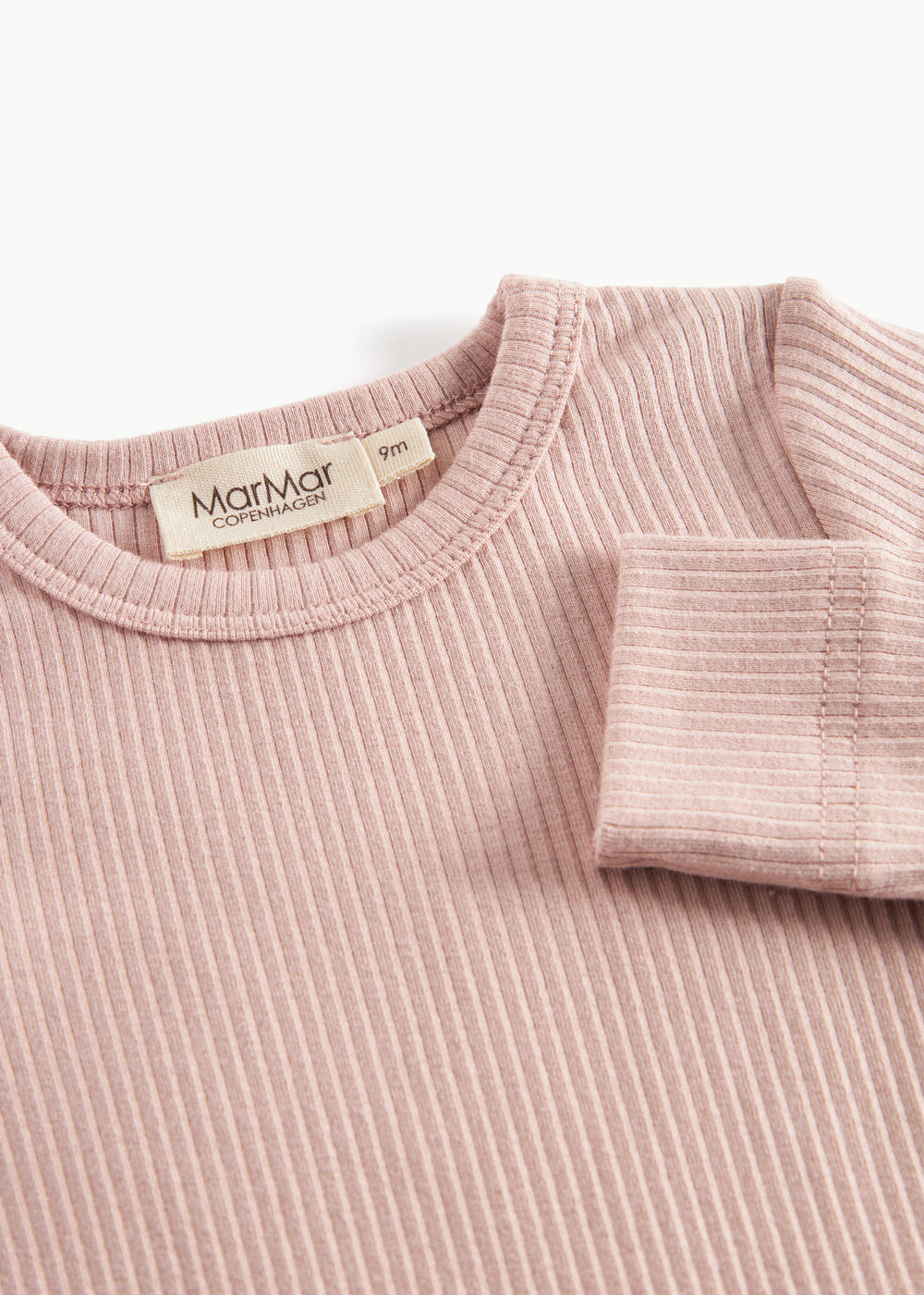 Nærbillede af ribstrikket materiale og hals på lyserød body til børn