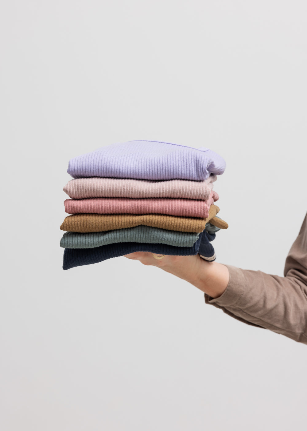 Person holder foldede børnetrøjer i forskellige farver, inkl. navyblå ribstrikket t-shirt