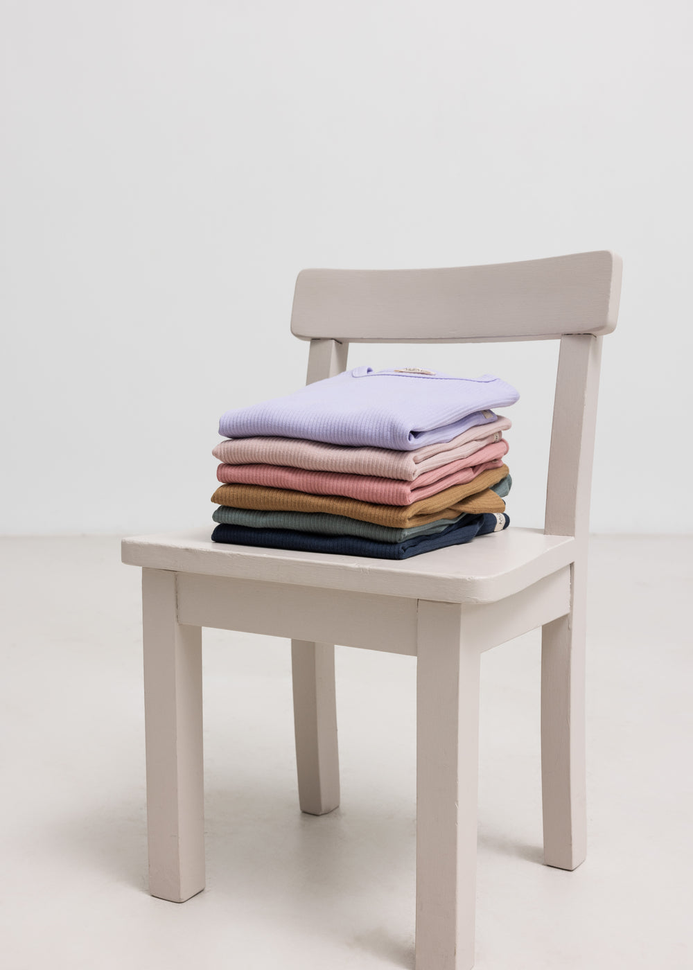 Stablet ribstrikket børnetøj i forskellige farver på en stol