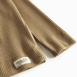 Nærbillede af ribstrikket stof og mærkat på brun børnetrøje