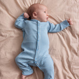 Baby iført blå og hvid stribet heldragt ligger på et beige tæppe