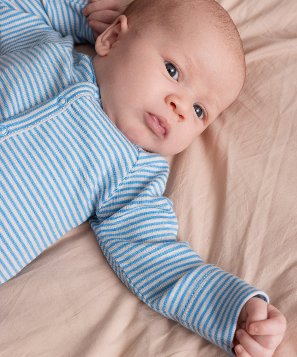 Baby iført blå og hvid stribet heldragt ligger på et beige tæppe