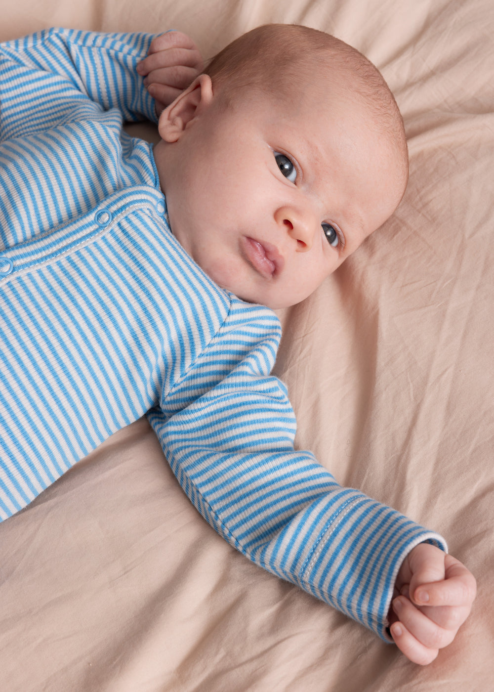 Baby iført blå og hvid stribet heldragt ligger på et beige tæppe