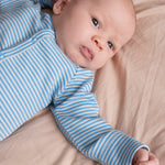 Baby iført blå- og hvidstribet body med lange ærmer, liggende på beige tæppe