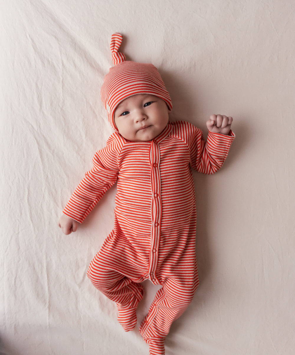 Baby iført rød og hvid stribet hue og heldragt liggende på ryggen