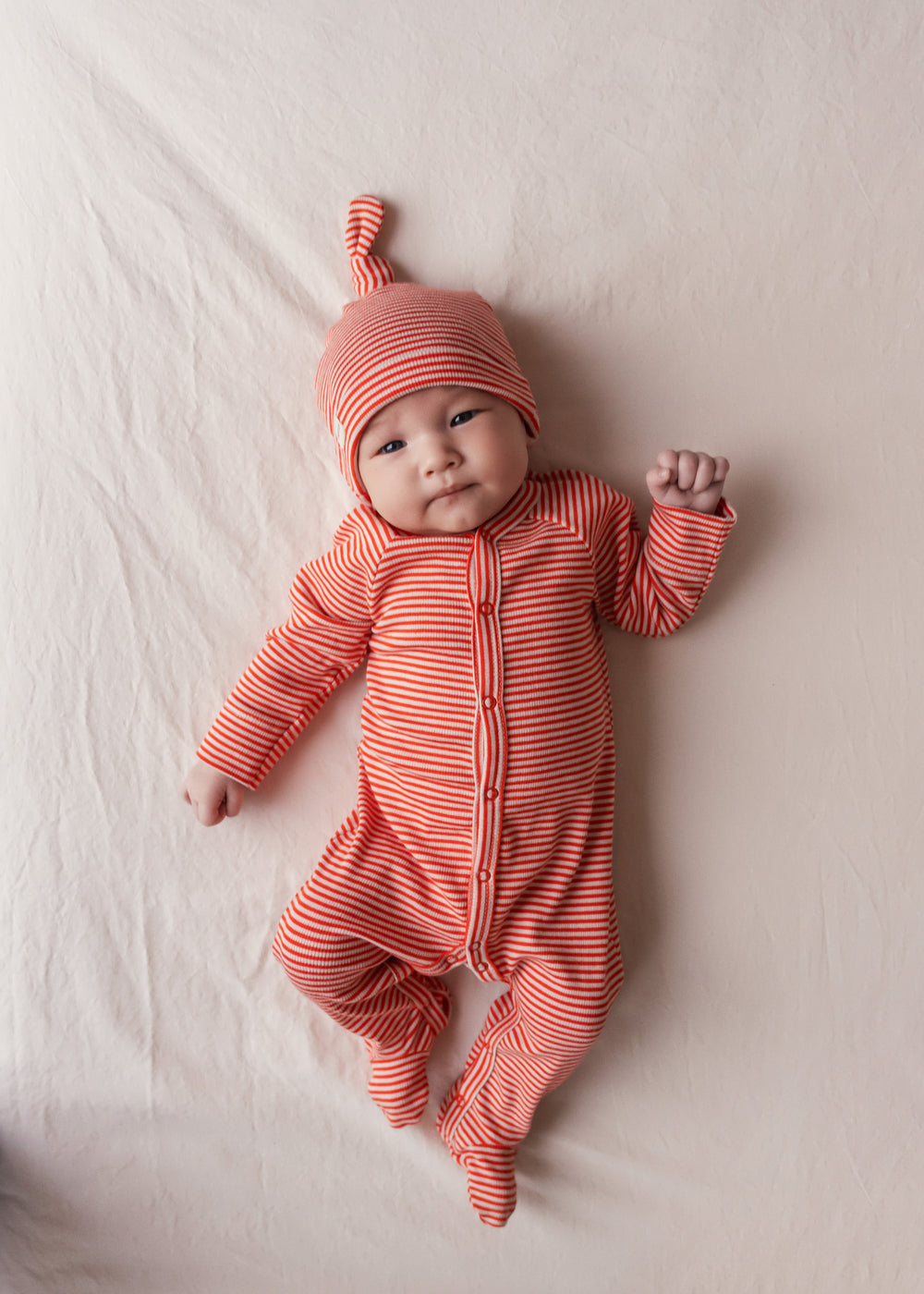 Baby iført rød heldragt og hue ligger på et tæppe