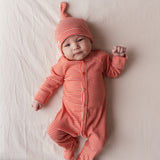 Baby iført rød heldragt og hue ligger på et tæppe