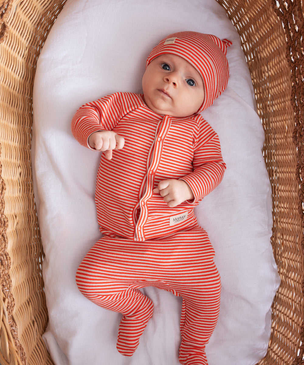 Baby iført koralfarvet stribet sæt med hue, cardigan og bukser i en fletkurv