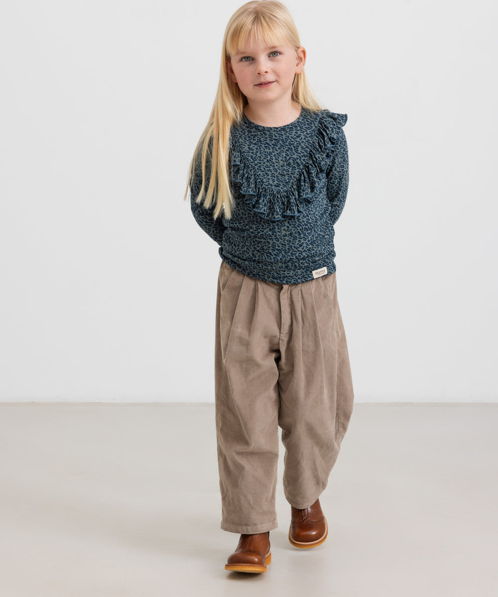 Pige iført mørkeblå leopardmønstret bluse med flæser og beige bukser
