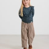 Pige iført mørkeblå leopardmønstret bluse med flæser og beige bukser