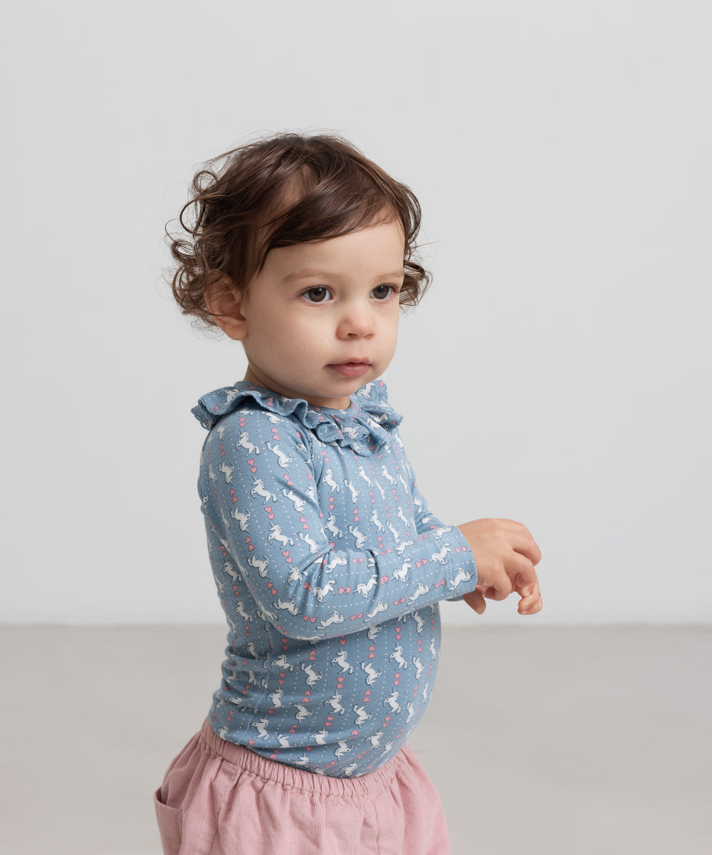 Baby iført blå body med enhjørningemønster og flæsekrave