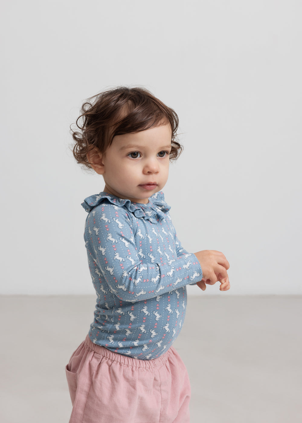 Baby iført lyserøde bukser og blå bluse med unicornprint