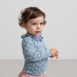 Baby iført lyserøde bukser og blå bluse med unicornprint