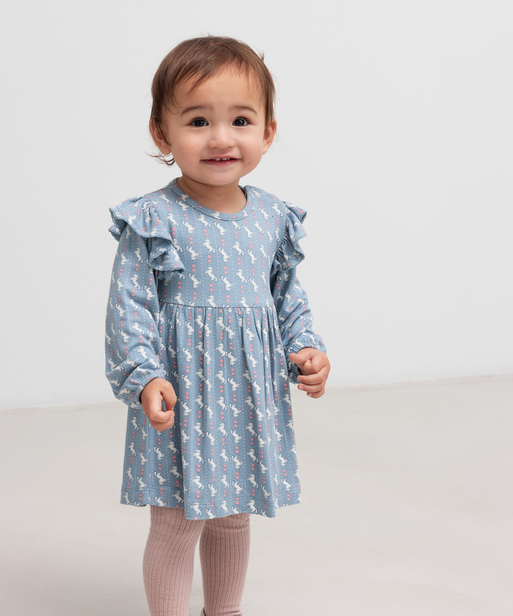 Baby iført blå kjole-body med enhjørningemønster