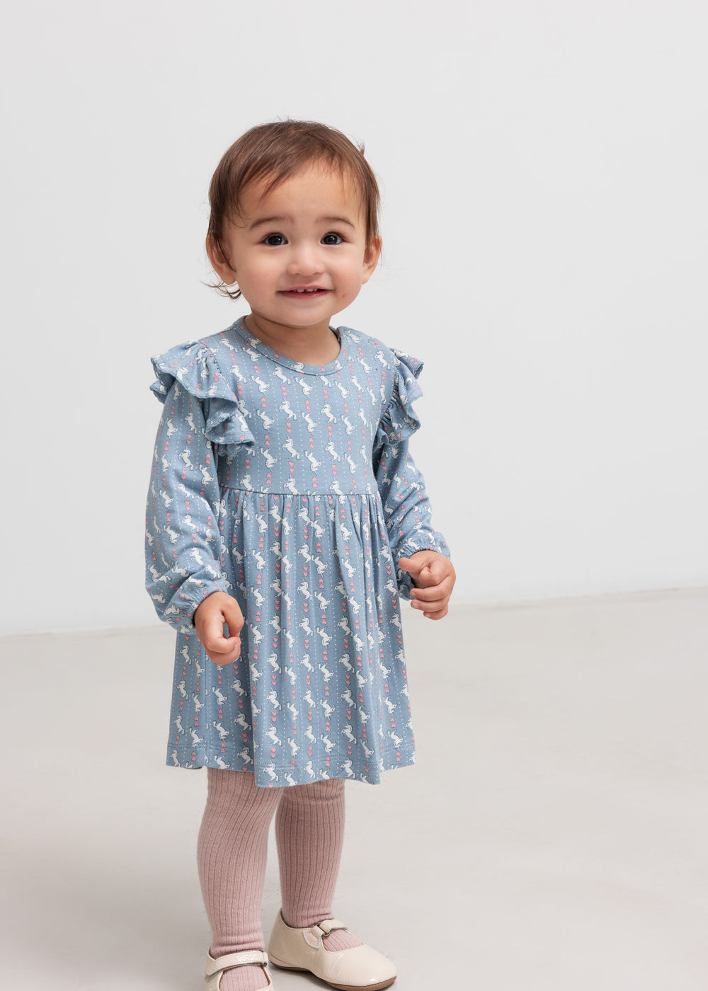 Baby iført blå kjole-body med enhjørningemønster