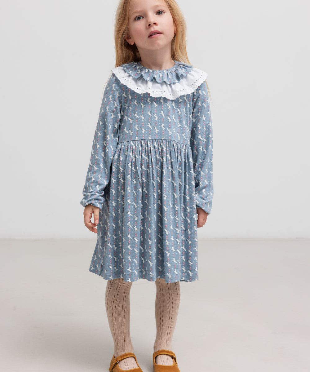Pige iført blå kjole med enhjørningemønster og flæsekrave