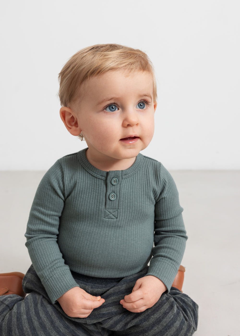 Baby iført grøn ribbody med lange ærmer og knaplukning