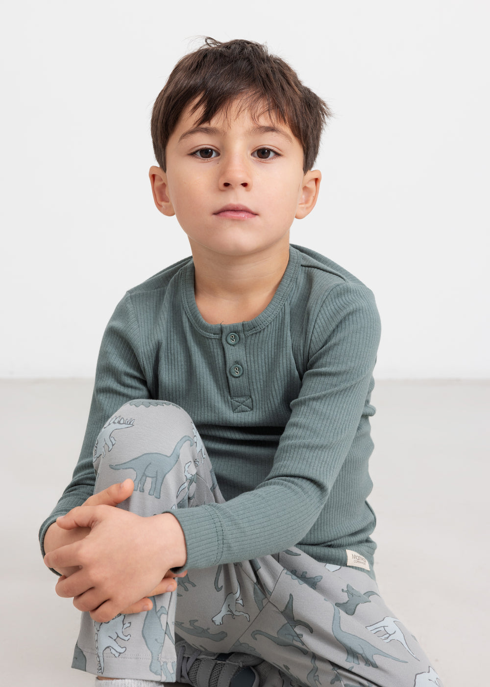 Dreng iført grøn ribbluse med knapper sidder på gulvet