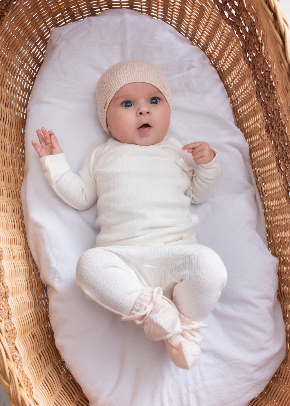 Baby iført hvide pointelle bukser og body liggende i en kurv