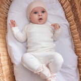 Baby iført hvide pointelle bukser og body liggende i en kurv