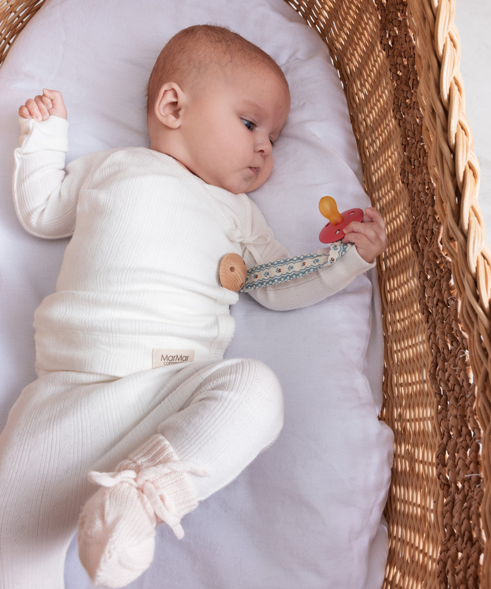 Baby iført hvid pointelle slå-om bluse og bukser liggende i kurv