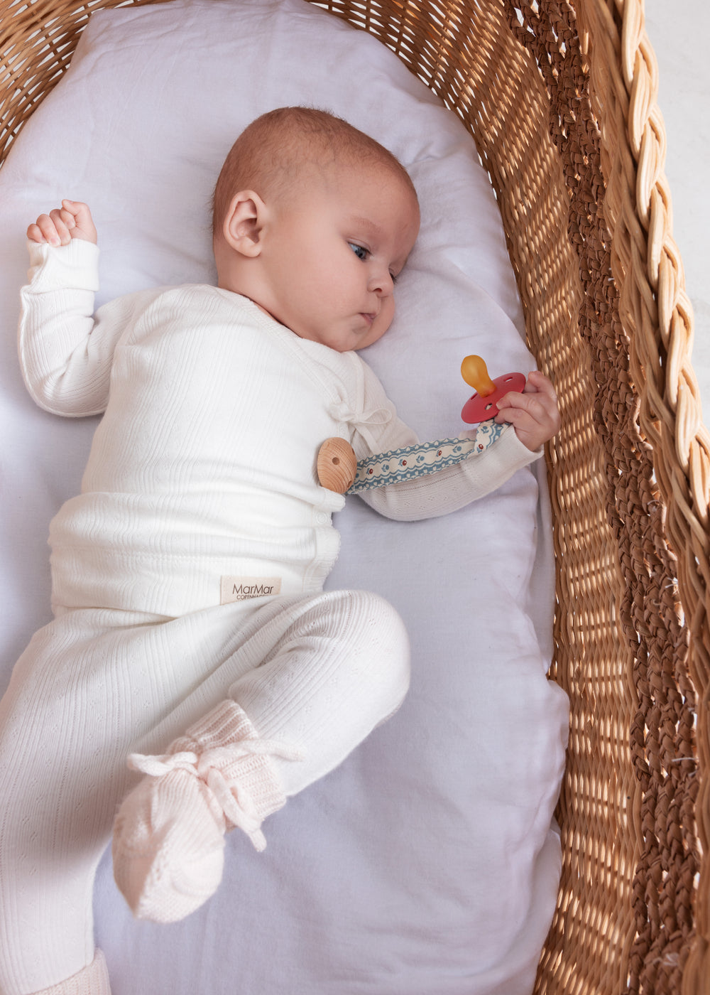 Baby iført hvid pointelle slå-om bluse og bukser liggende i kurv