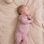 Baby iført rosa pointelle heldragt med fødder liggende på seng