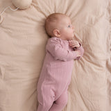 Baby iført rosa pointelle heldragt med fødder liggende på seng