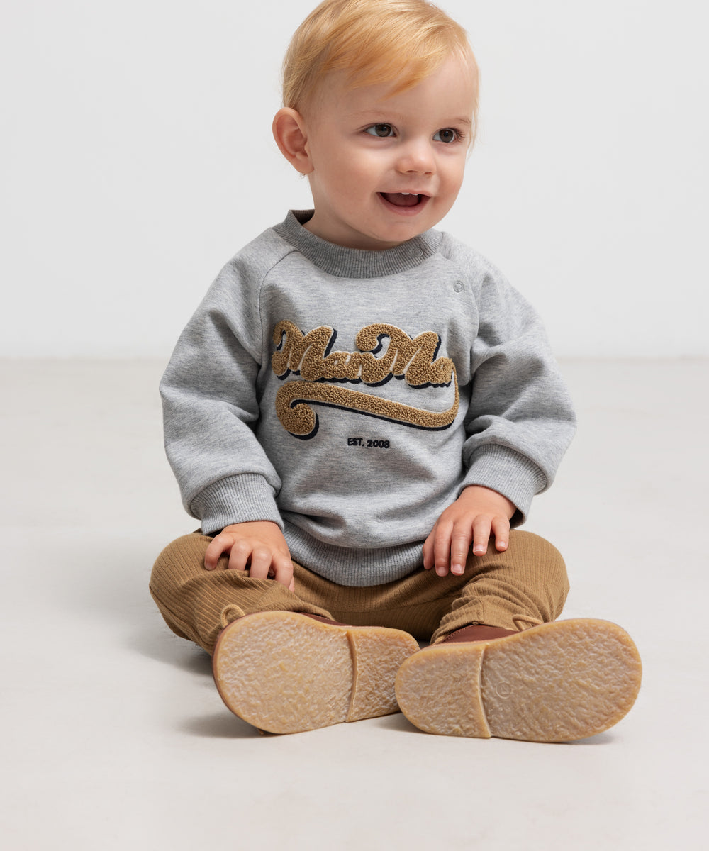 Siddende barn i grå sweatshirt med guld broderi