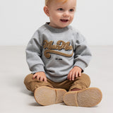 Siddende barn i grå sweatshirt med guld broderi