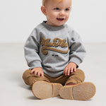 Baby iført brune ribstrikkede bukser och grå sweatshirt