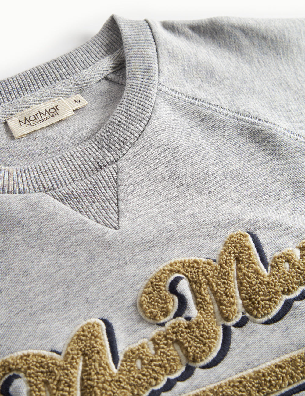 Nærbillede af gyldent broderi på grå sweatshirt til børn