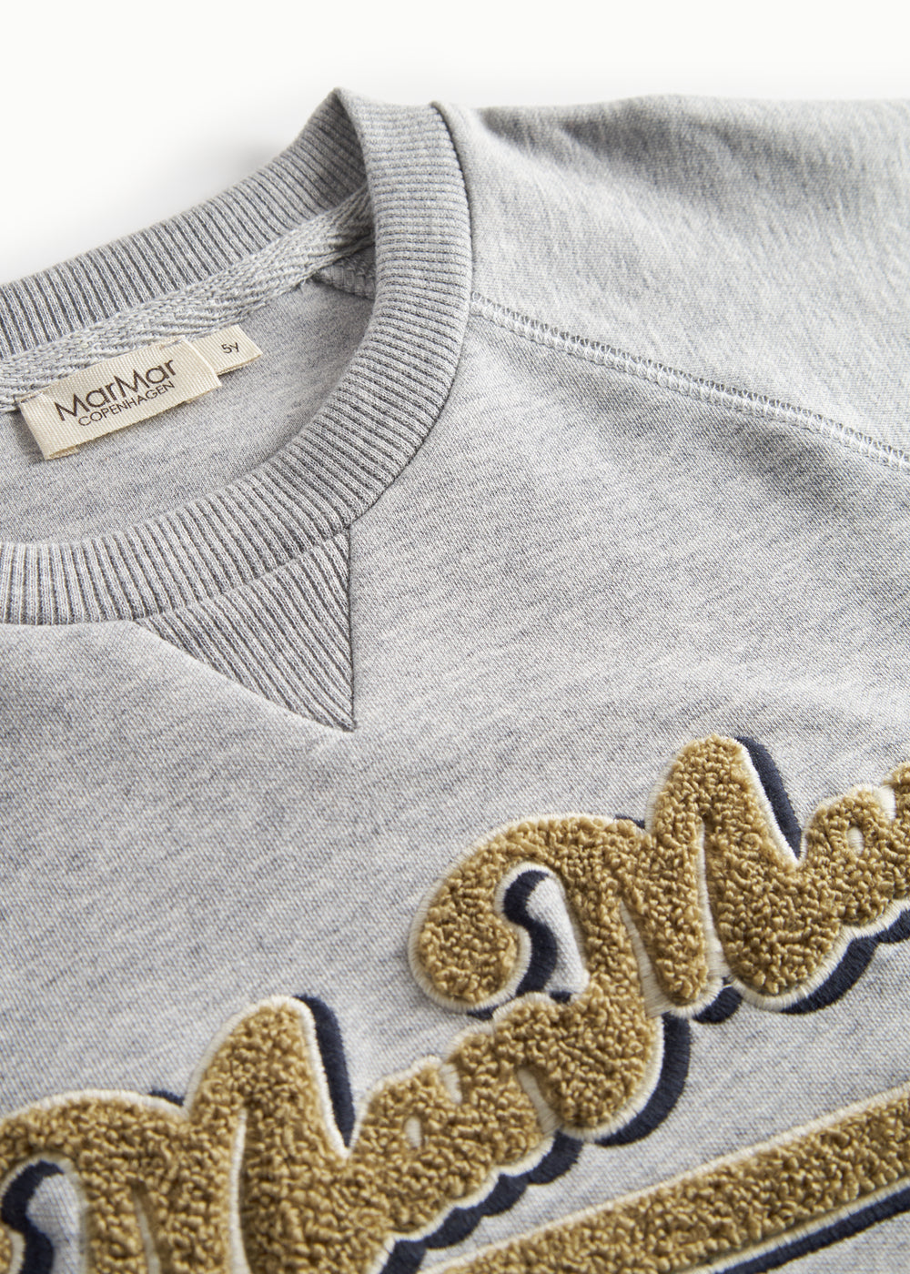 Nærbillede af gyldent broderi på grå sweatshirt til børn