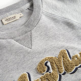 Nærbillede af gyldent broderi på grå sweatshirt til børn