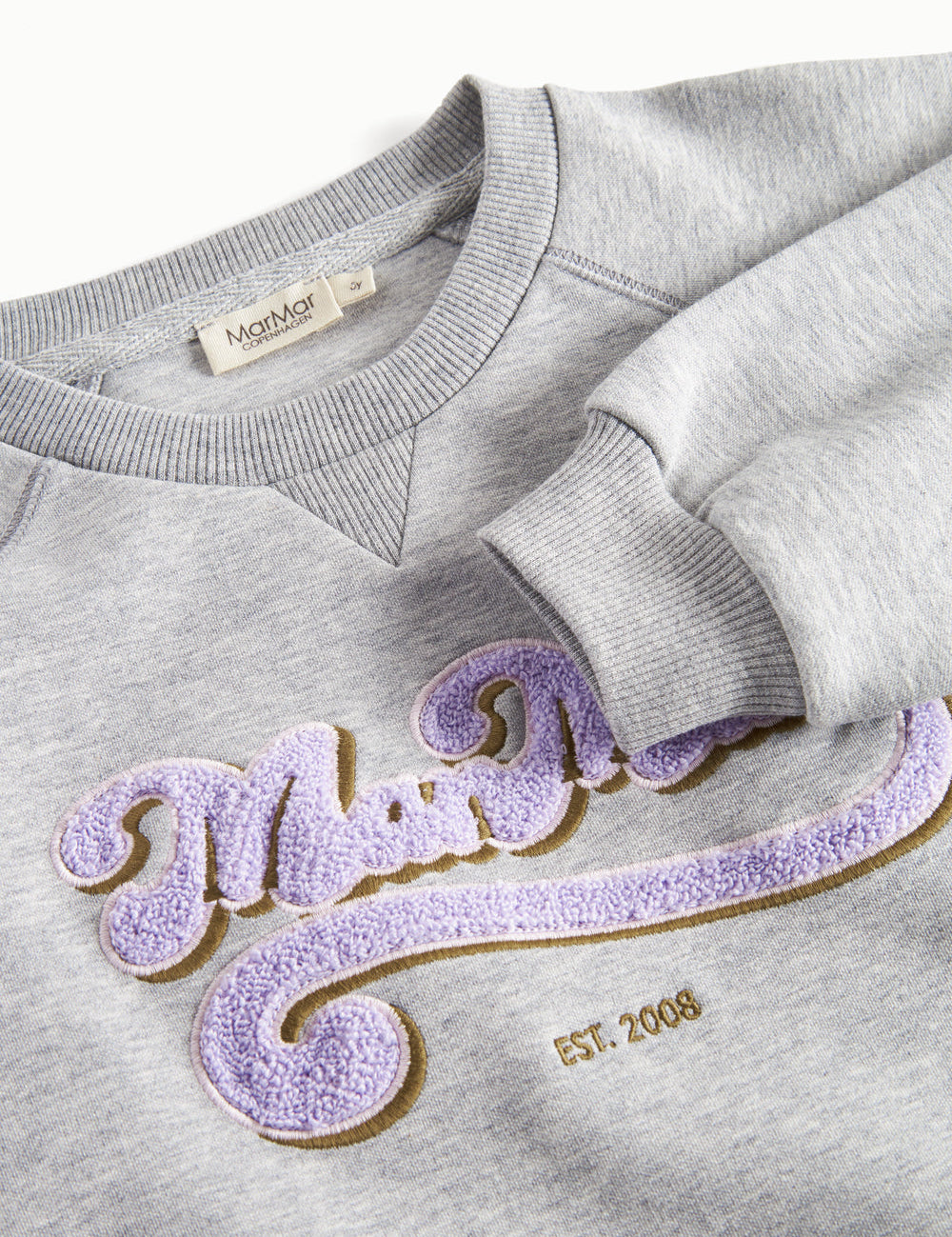 Nærbillede af lila broderet logo på grå sweatshirt til børn
