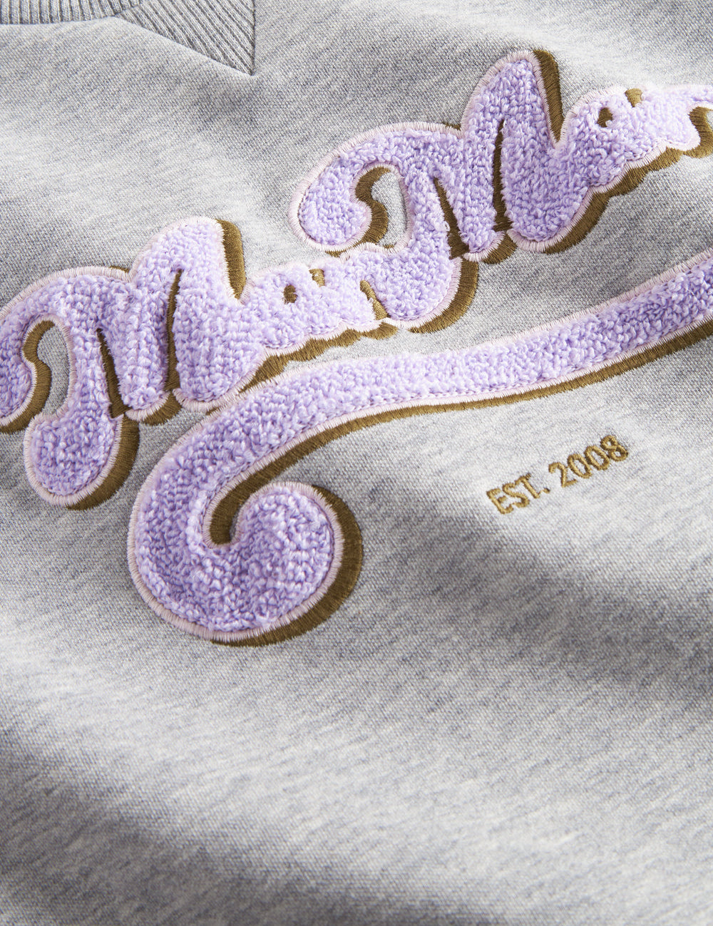 Nærbillede af lila broderet logo på grå sweatshirt til børn