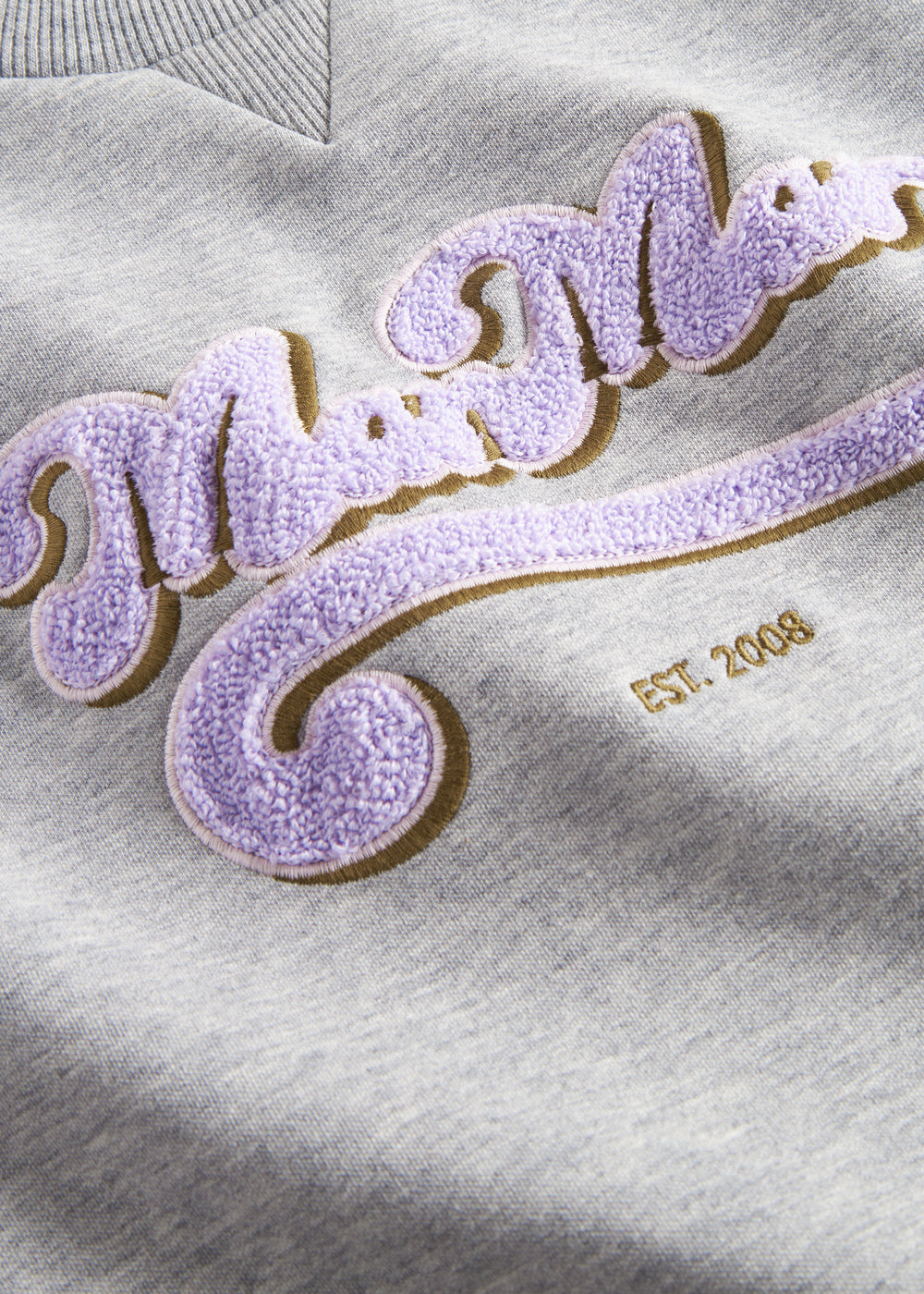 Nærbillede af lila broderet logo på grå sweatshirt til børn