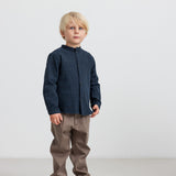 Dreng iført mørkeblå skjorte og brune bukser stående