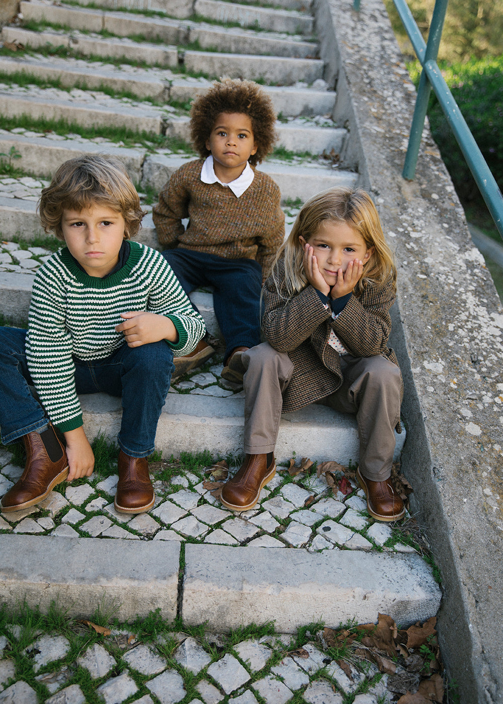 Gruppe børn i striktrøjer og jakker udendørs siddende på trapper