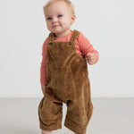 Baby iført brun fløjlsoverall og lyserød bluse