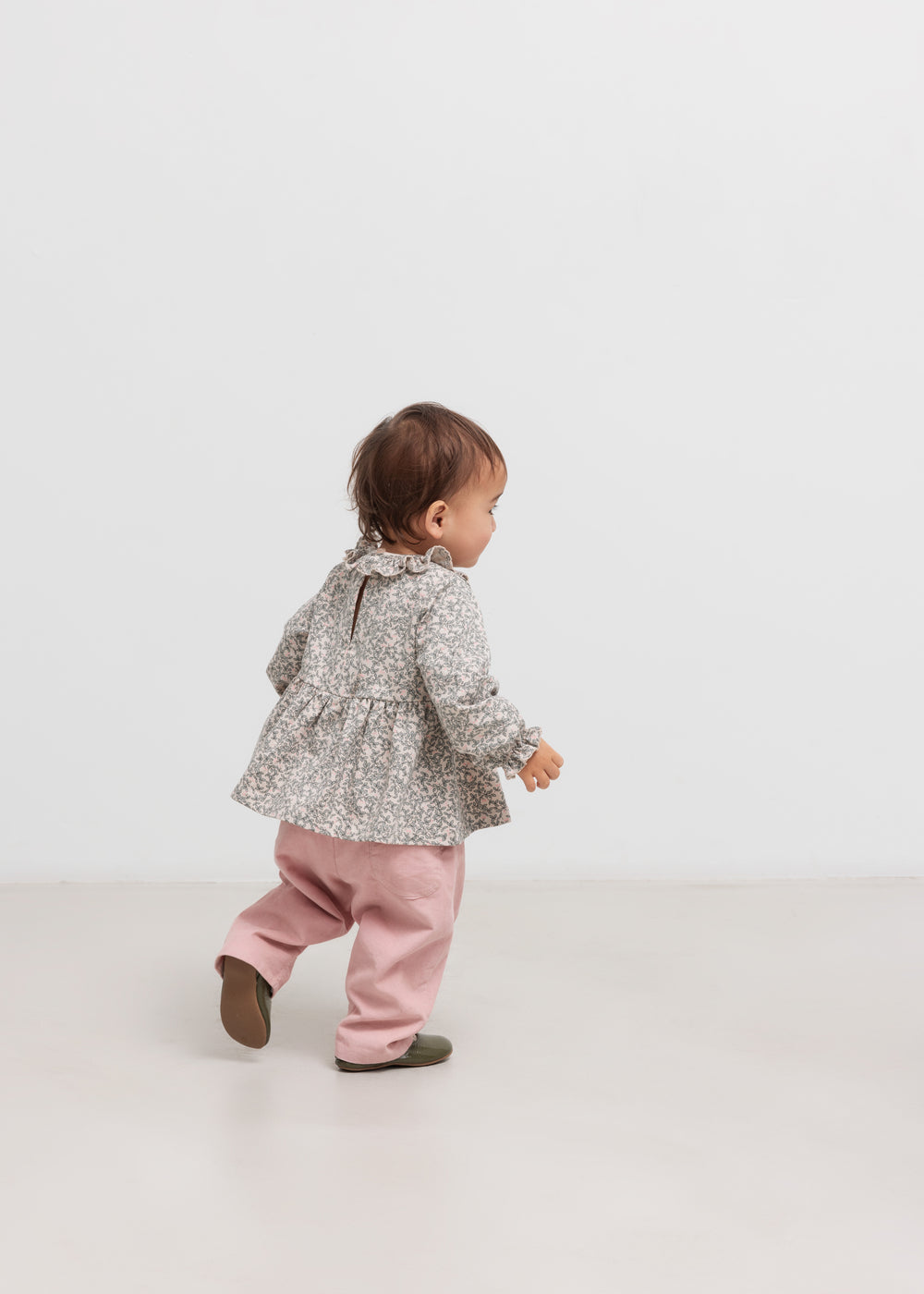 Baby iført lyserøde bukser og grå bluse set bagfra