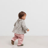 Baby iført lyserøde bukser og grå bluse set bagfra