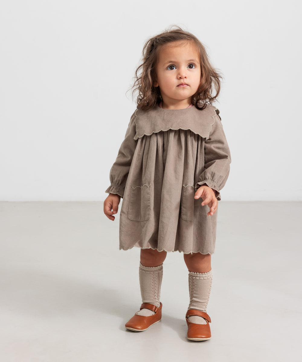 Pige iført beige babyfløjlskjole med lommer og lange ærmer