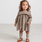 Pige iført beige babyfløjlskjole med lommer og lange ærmer