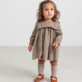 Pige iført beige babyfløjlskjole med lommer og lange ærmer