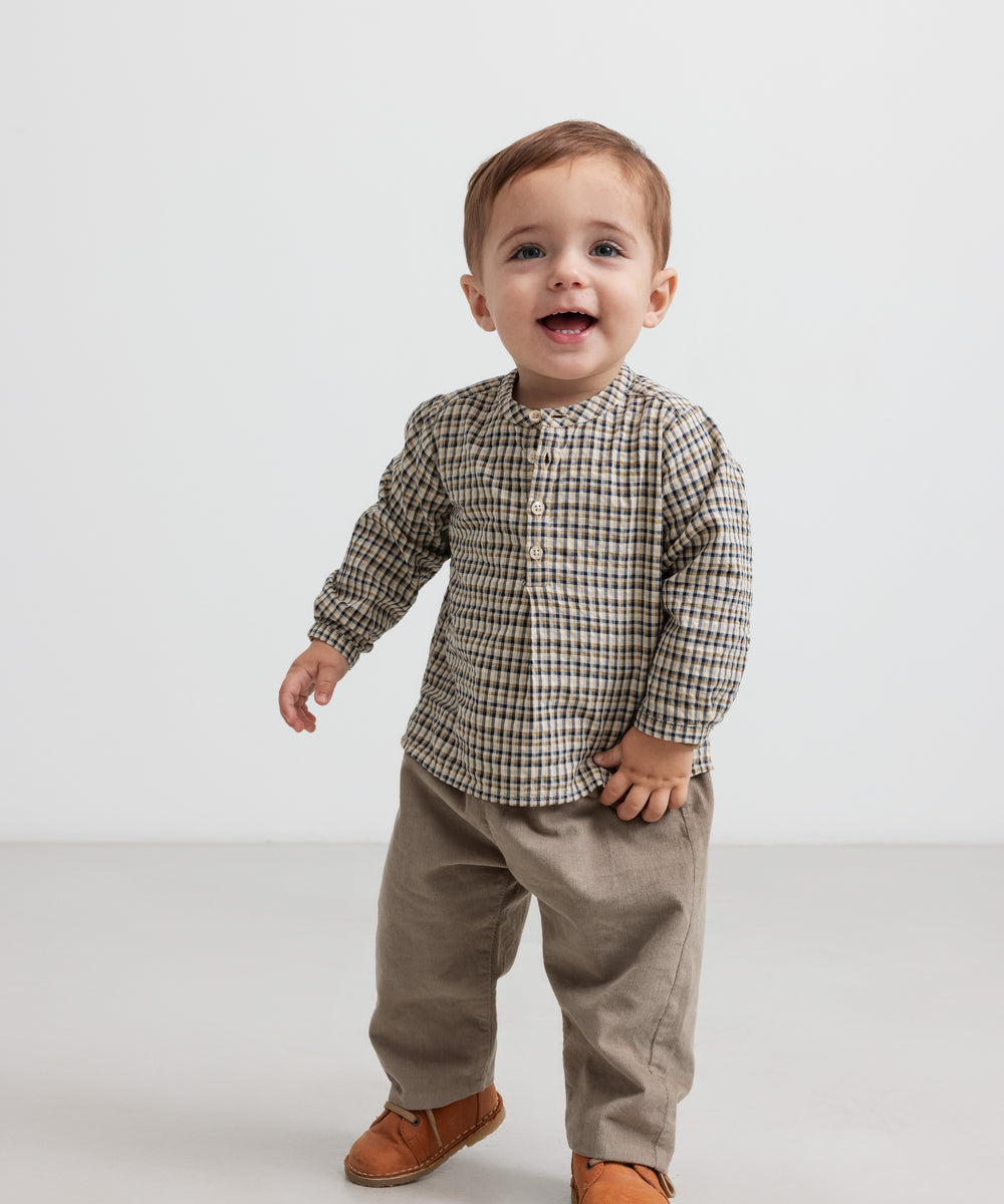 Baby iført beige babyfløjl­sbukser og bluse