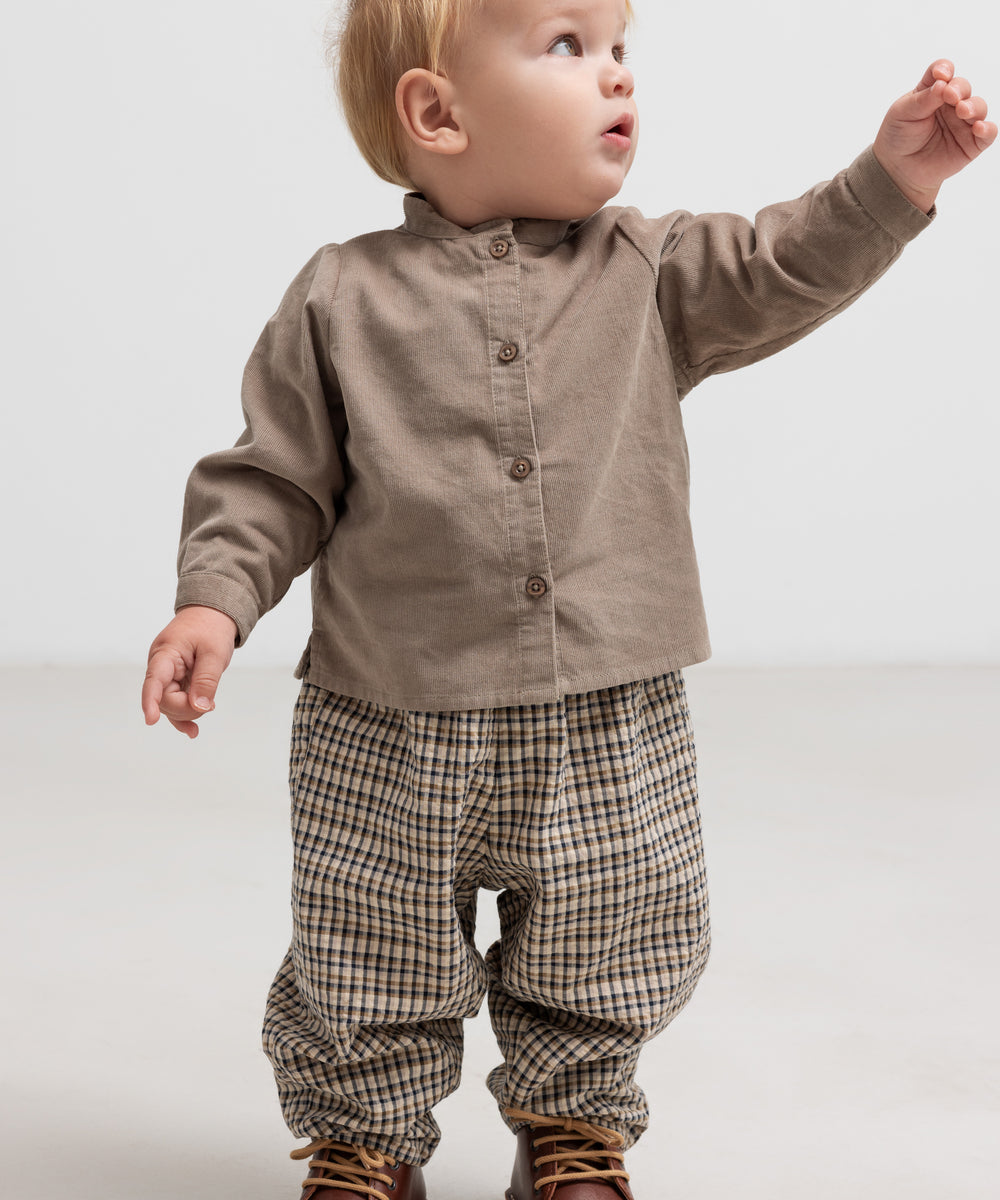 Baby iført beige babyfløjlsskjorte og ternede bukser