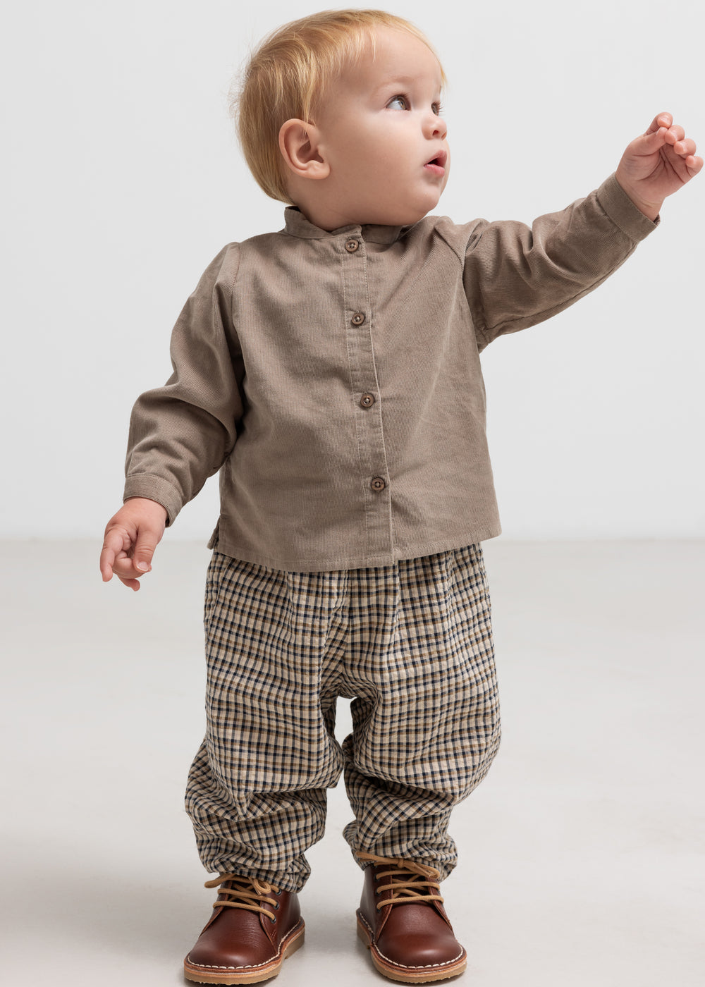 Baby iført beige babyfløjlsskjorte og ternede bukser