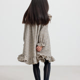 Pige iført brun ternet strikkjole med flæser foran